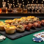 Elegant platter with mini quiches, stuffed mushrooms, and bacon-wrapped dates on black slate over green casino felt, accented by poker chips, dice, and face-down playing cards, with a blurred self-serve cocktail station and string lights behind.